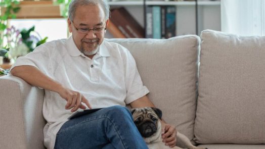 older man sits on couch with pug following a Bible reading plan on his tablet